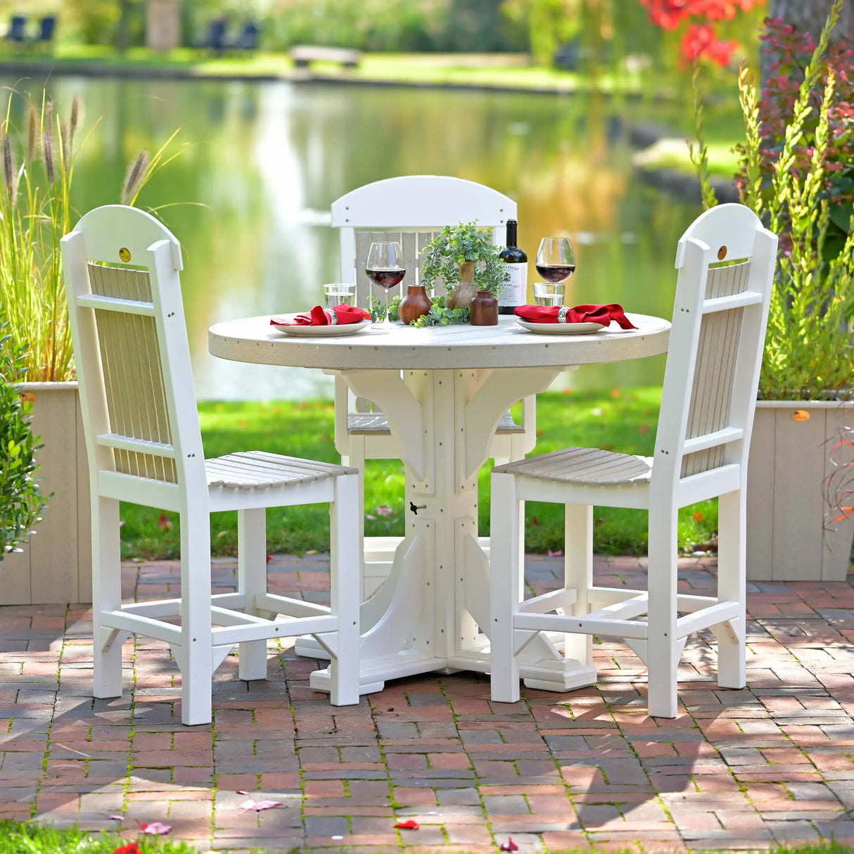 This is a lifestyle image showing three Birch and White colored Side Chairs with a matching table between them. There are plates and napkins and wine glasses on the table and a body of water in the background.