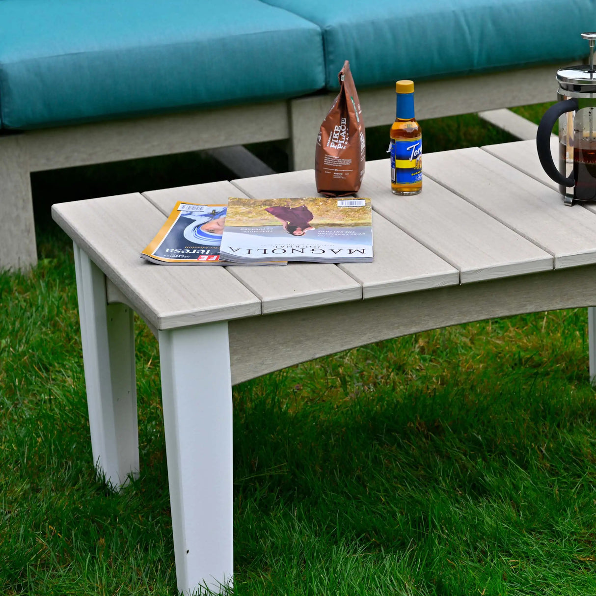 This is a lifestyle image showing the Weatherwood and White colored coffee table in front of a birch colored sofa with a teal seat cushion on it.
