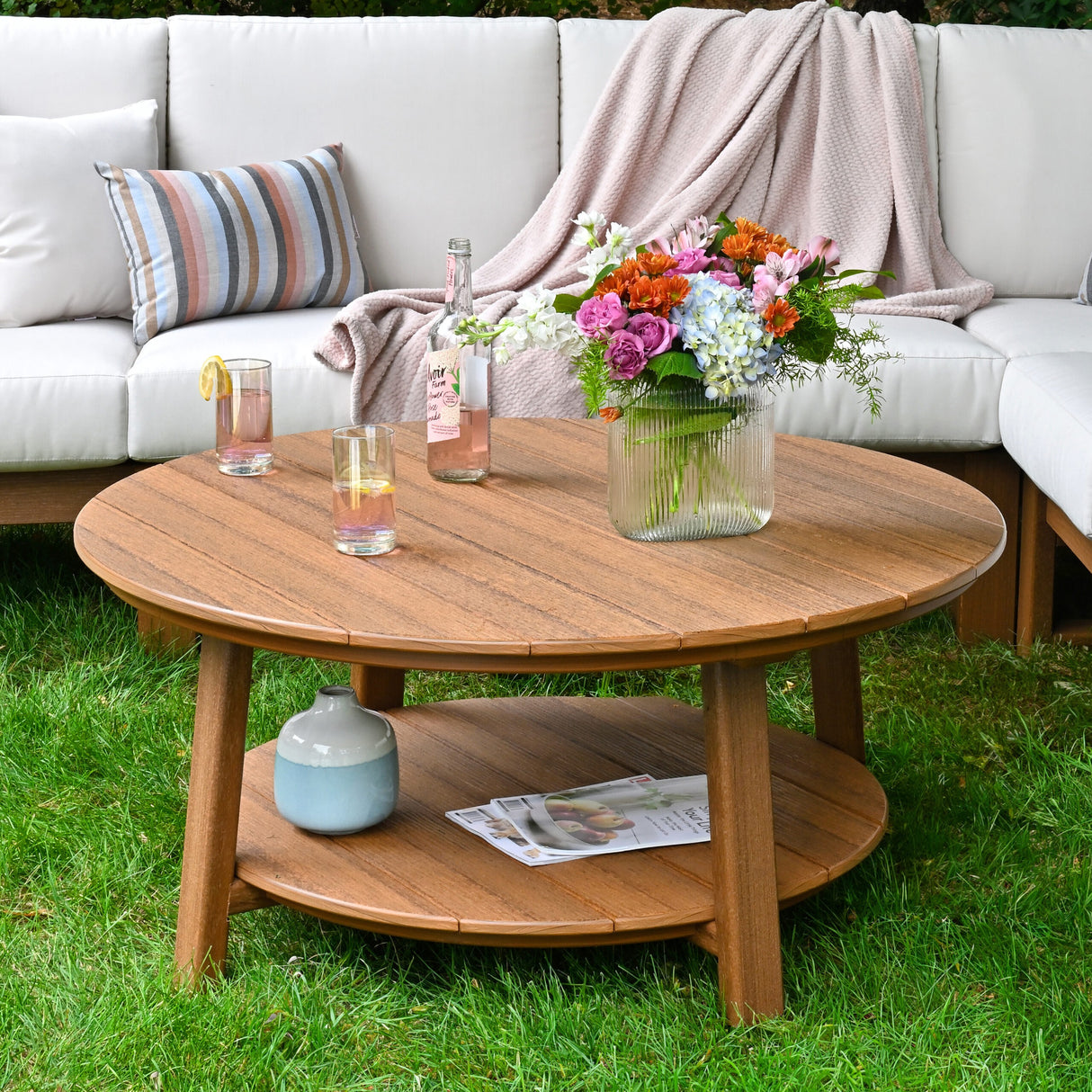 This is a lifestyle image showing the Antique Mahogany colored conversation table in front of an outdoor sectional sofa. There are two glasses on the table next to a vase of flowers.