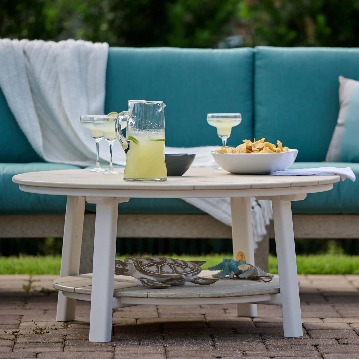 This is a lifestyle image showing the Birch and White colored conversation table in front of an outdoor sofa with teal colored seat cushions.