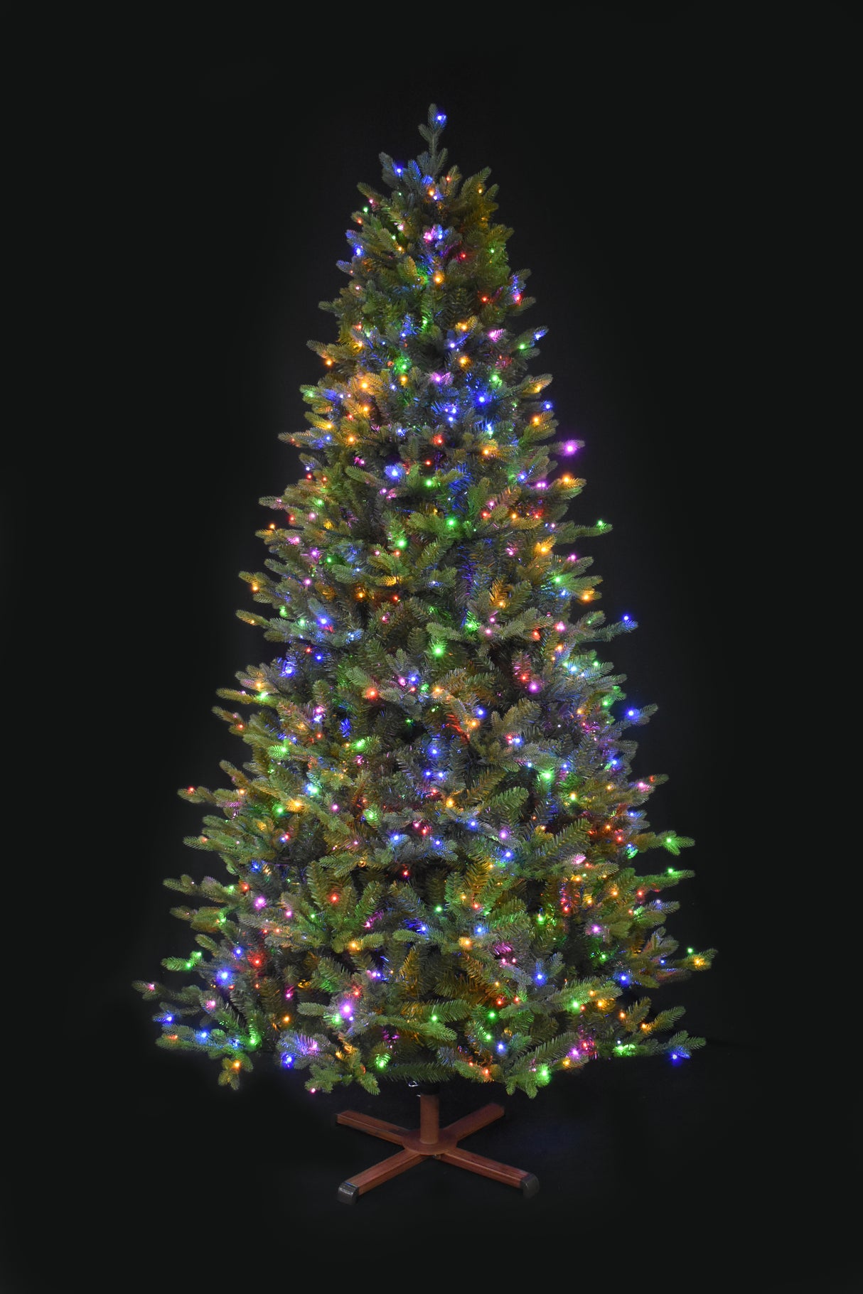 This image shows the tree with Multi-Colored Starry Lights. It has a wooden stand. This tree is shown against a black background.