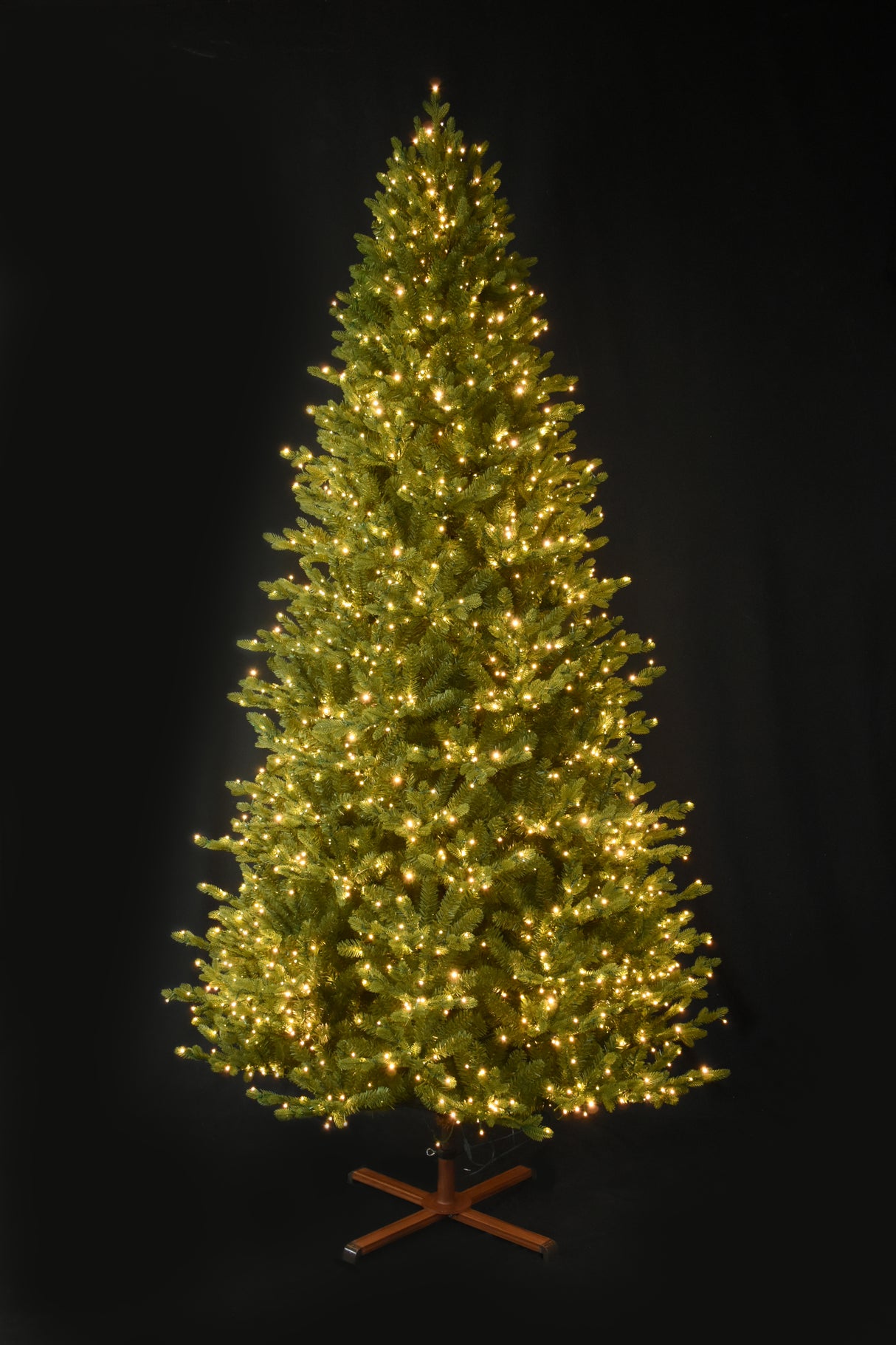 This image shows the tree pre-lit with Warm White Starry Lights. It has a wooden tree stand. This shows the tree on a black background.