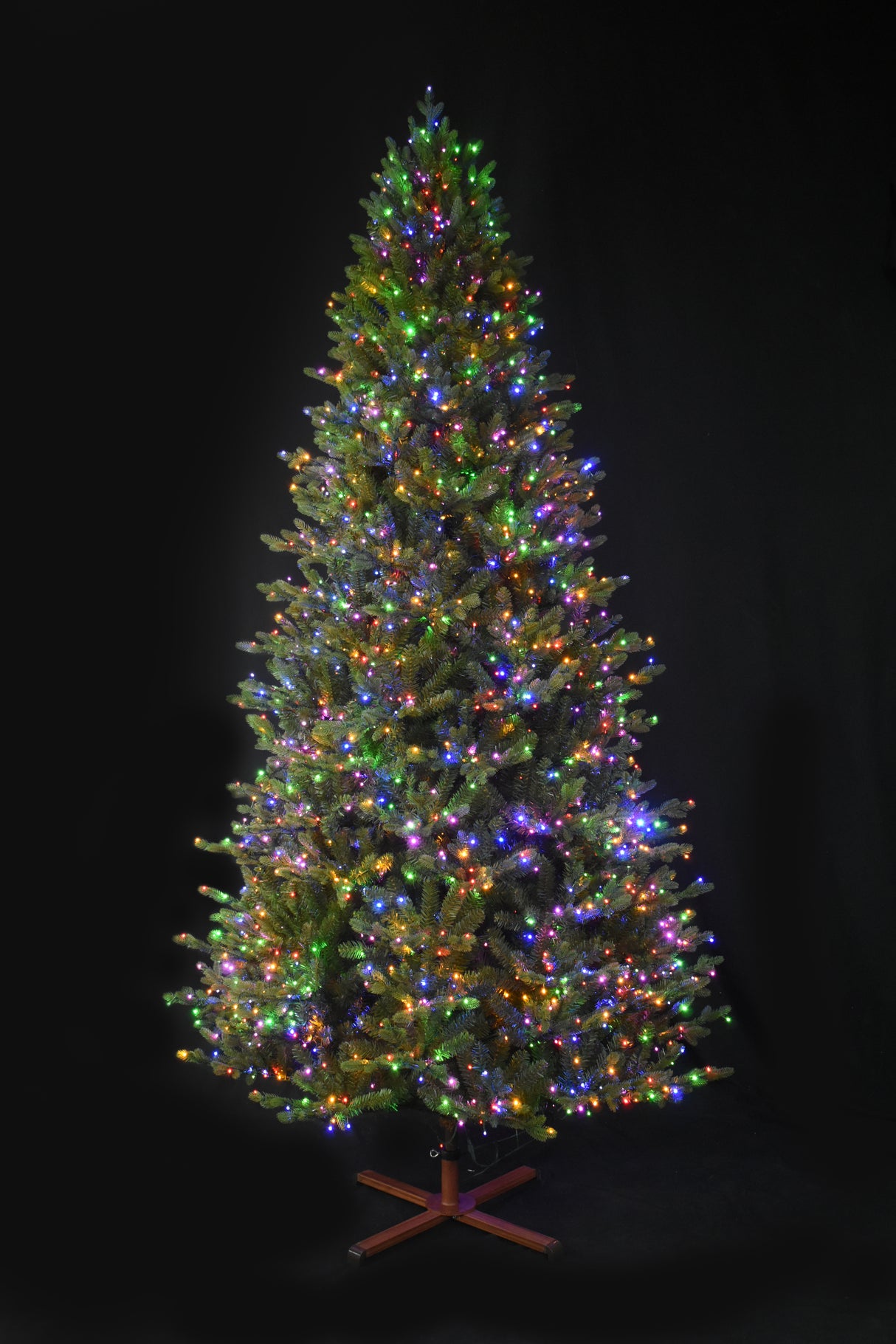 This image shows the tree with Multi-Colored Starry Lights. It has a wooden stand. This tree is shown against a black background.
