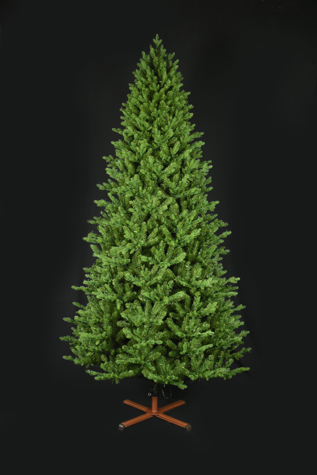 This image shows the tree with the lights turned off. It has a wooden stand. This tree is shown against a black background.