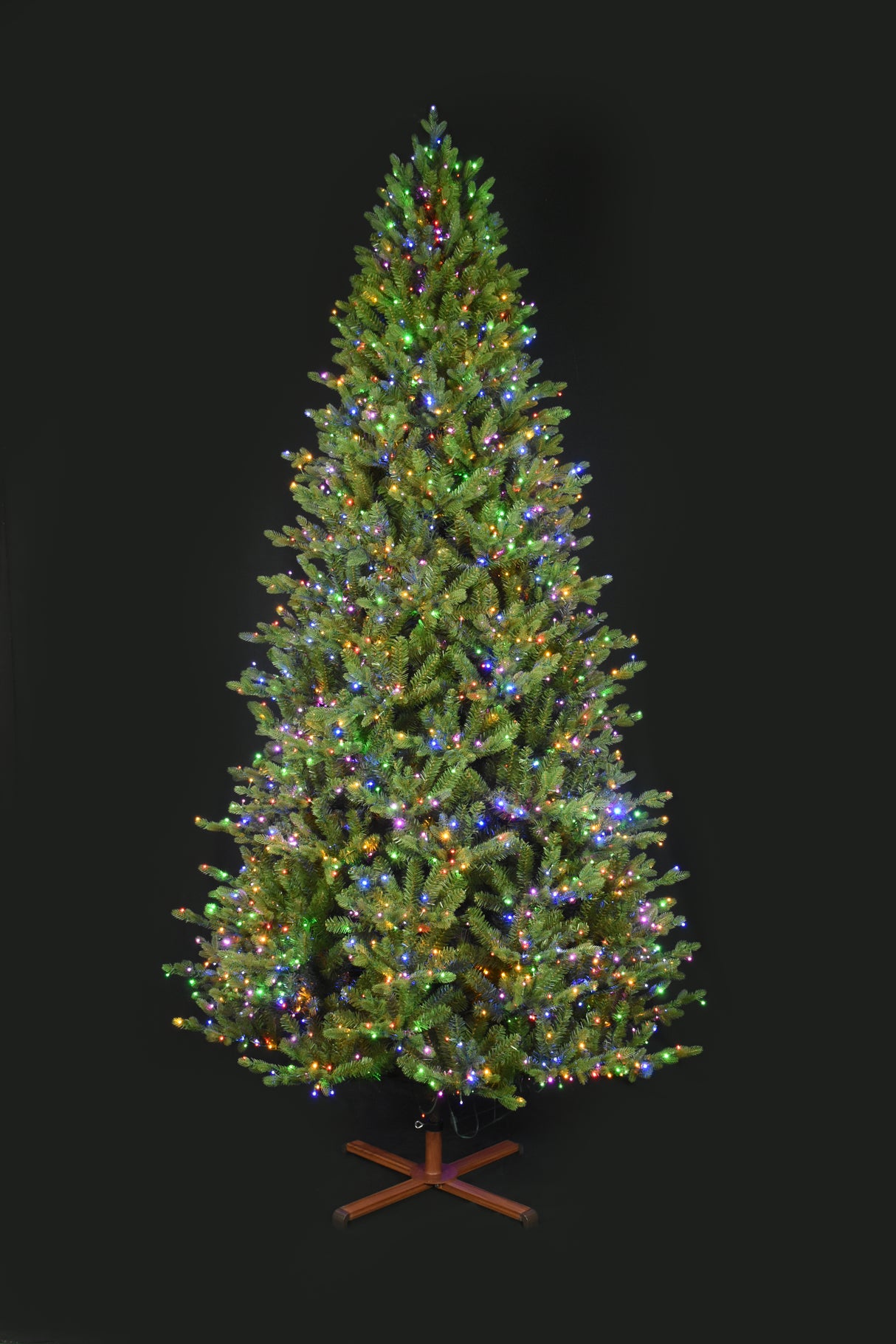 This image shows the tree with Multi-Colored Starry Lights. It has a wooden stand. This tree is shown against a black background.