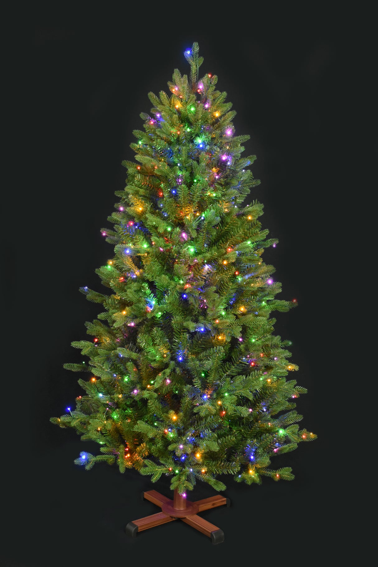 This image shows the tree with Multi-Colored Starry Lights. It has a wooden stand. This tree is shown against a black background.