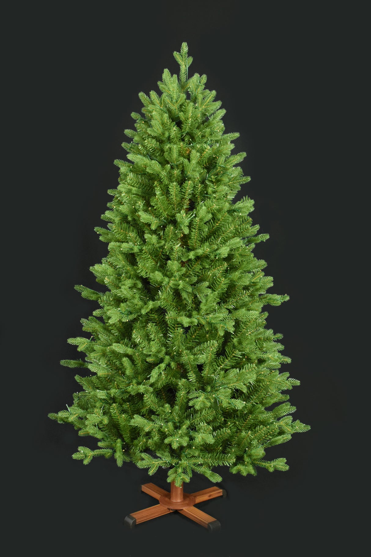 This image shows the tree with the lights turned off. It has a wooden stand. This tree is shown against a black background.