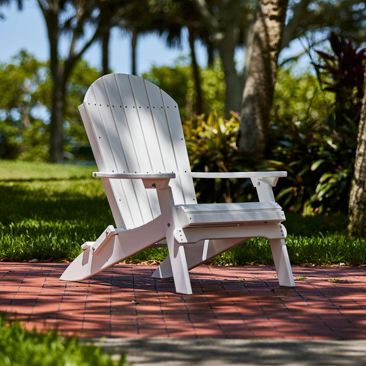 This is the White colored Folding Adirondack Chair on a brick patio in a grassy backyard.