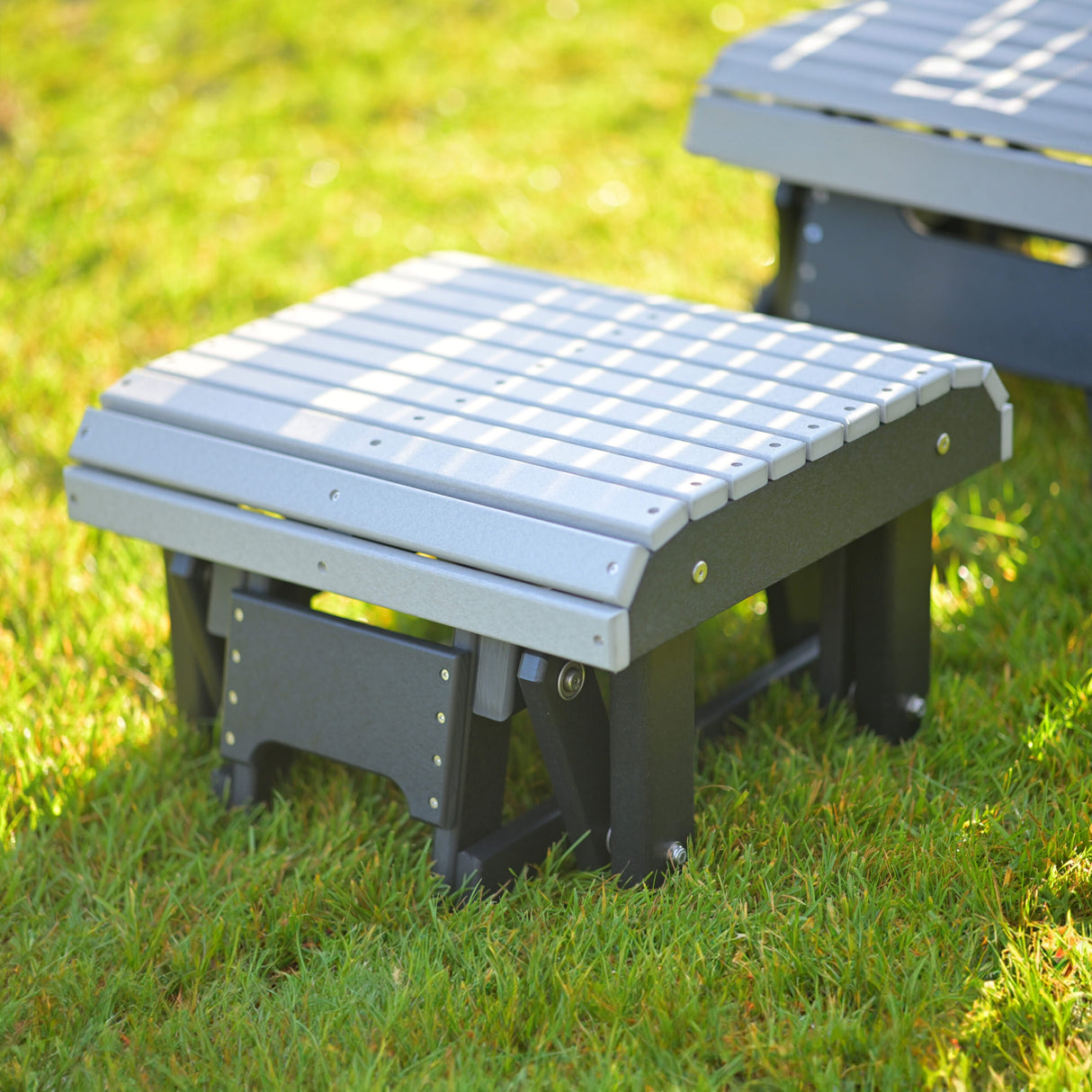 This is a lifestyle image showing the Dove Gray and Black colored glider footrest in front of a matching glider chair on some grass.