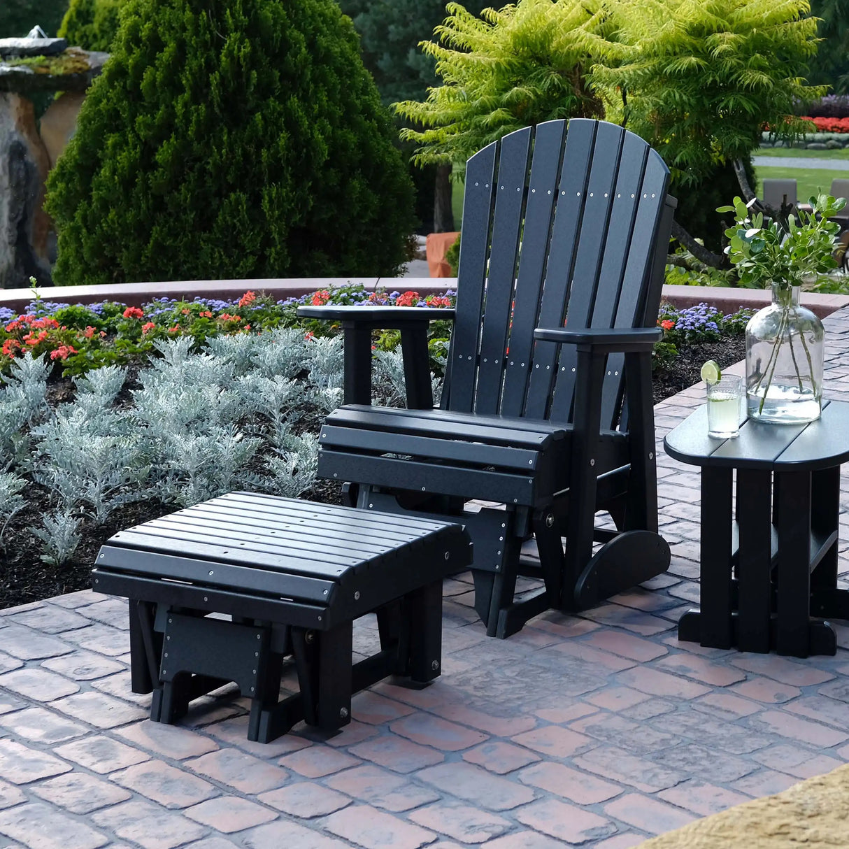 This is a lifestyle image showing the Black colored glider footrest in front of a matching Adirondack chair on a brick patio outside.