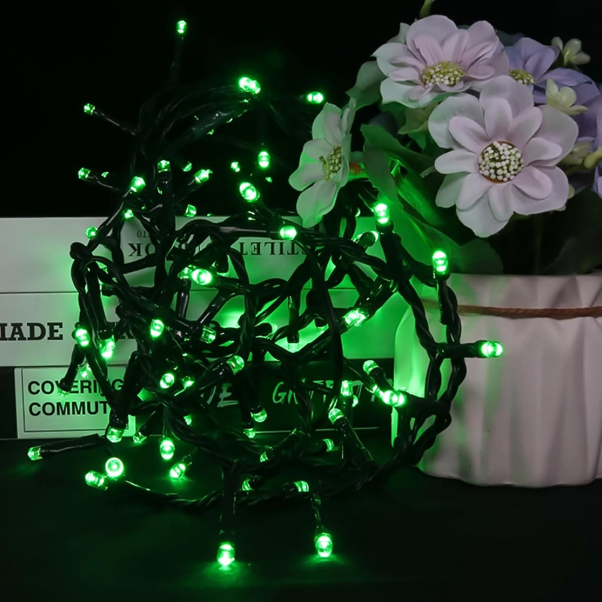 This is a lifestyle image showing the green starry lights on a table next to a pot of flowers.