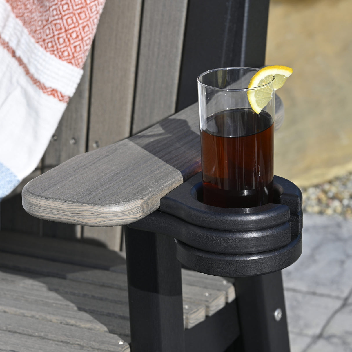 This is a lifestyle image showing the Black colored cup holder added onto the arm of a Coastal Gray and Black colored Adirondack chair.