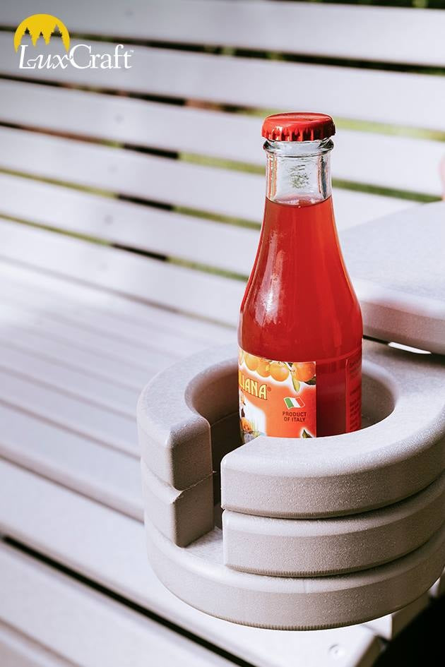 This is a lifestyle image showing the Weatherwood colored cup holder added onto a matching Adirondack chair. There's a bottle of orange soda in the cupholder.