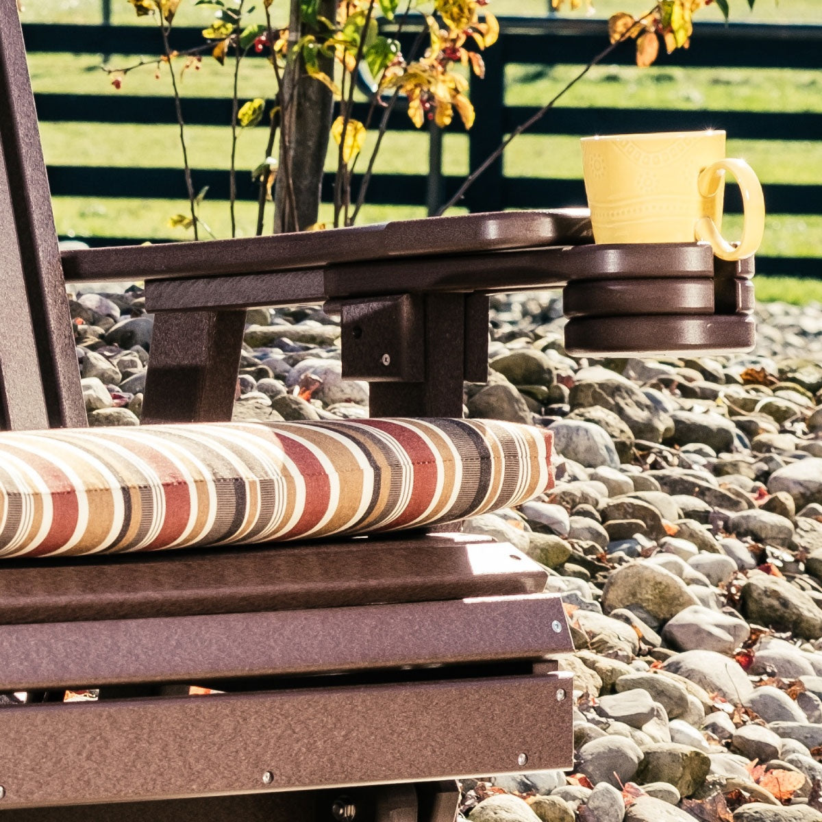This is a lifestyle image showing the Antique Mahogany colored cup holder added onto a matching chair. There's a yellow mug inside the cup holder.