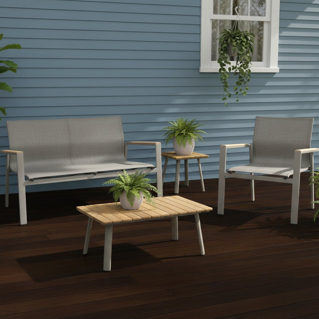 This is a lifestyle image showing this patio furniture set on a weathered wood back porch up against a blue house. There are small potted plants on the coffee table and the end table.
