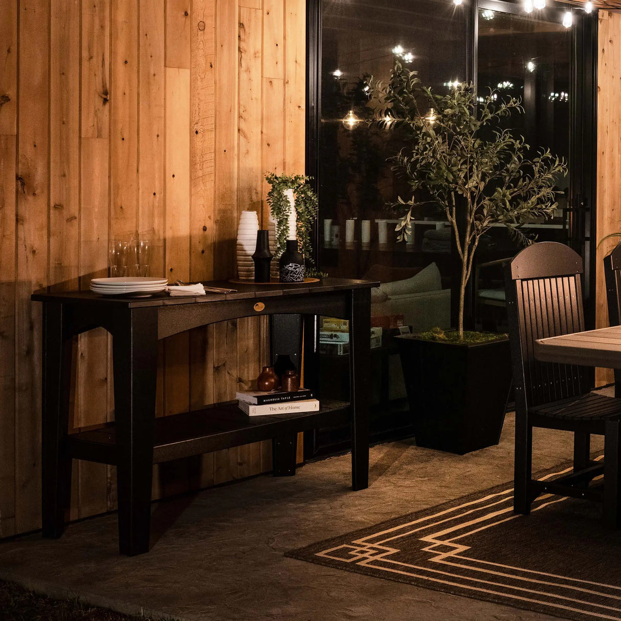 This is a lifestyle image showing the Black colored Island Buffet Table inside a dining room up against a wooden wall.