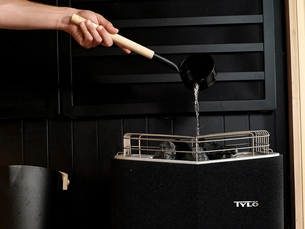 This image shows a person pouring water on the heat source inside the sauna.