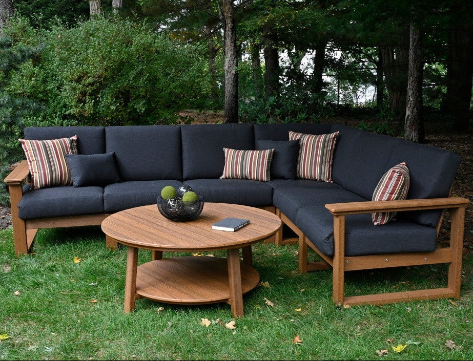 This is a lifestyle image showing the deep seating sectional set in a grassy backyard. The frames are antique mahogany and the cushions are spectrum carbon.