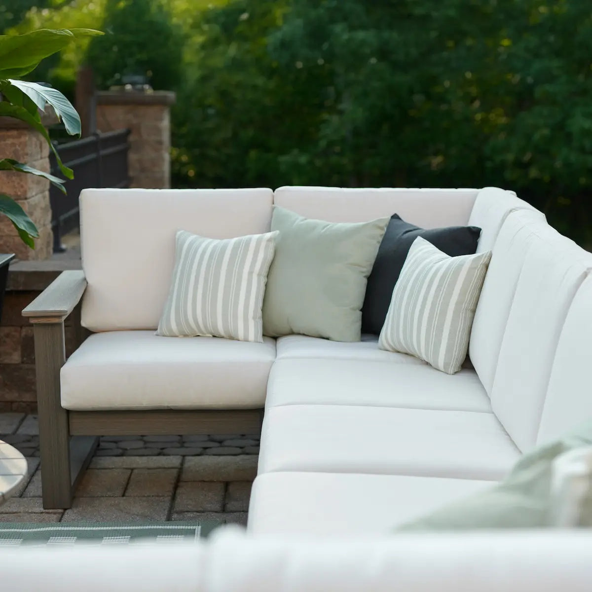 This is a lifestyle image showing the deep seating sectional set on a brick patio. The frames are coastal gray and the cushions are canvas.