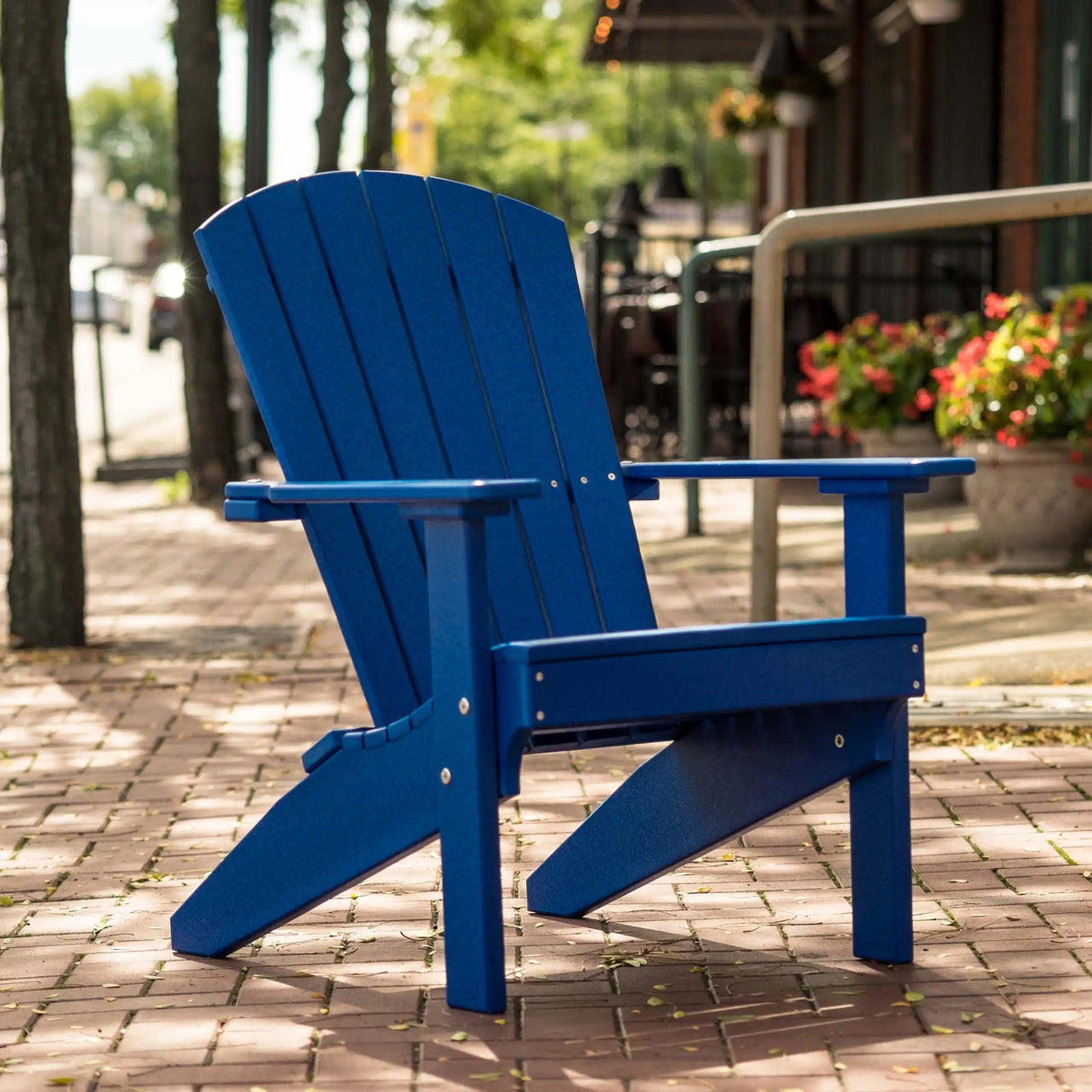 This is a lifestyle image showing the Blue colored Lakeside Adirondack Chair on a brick sidewalk.