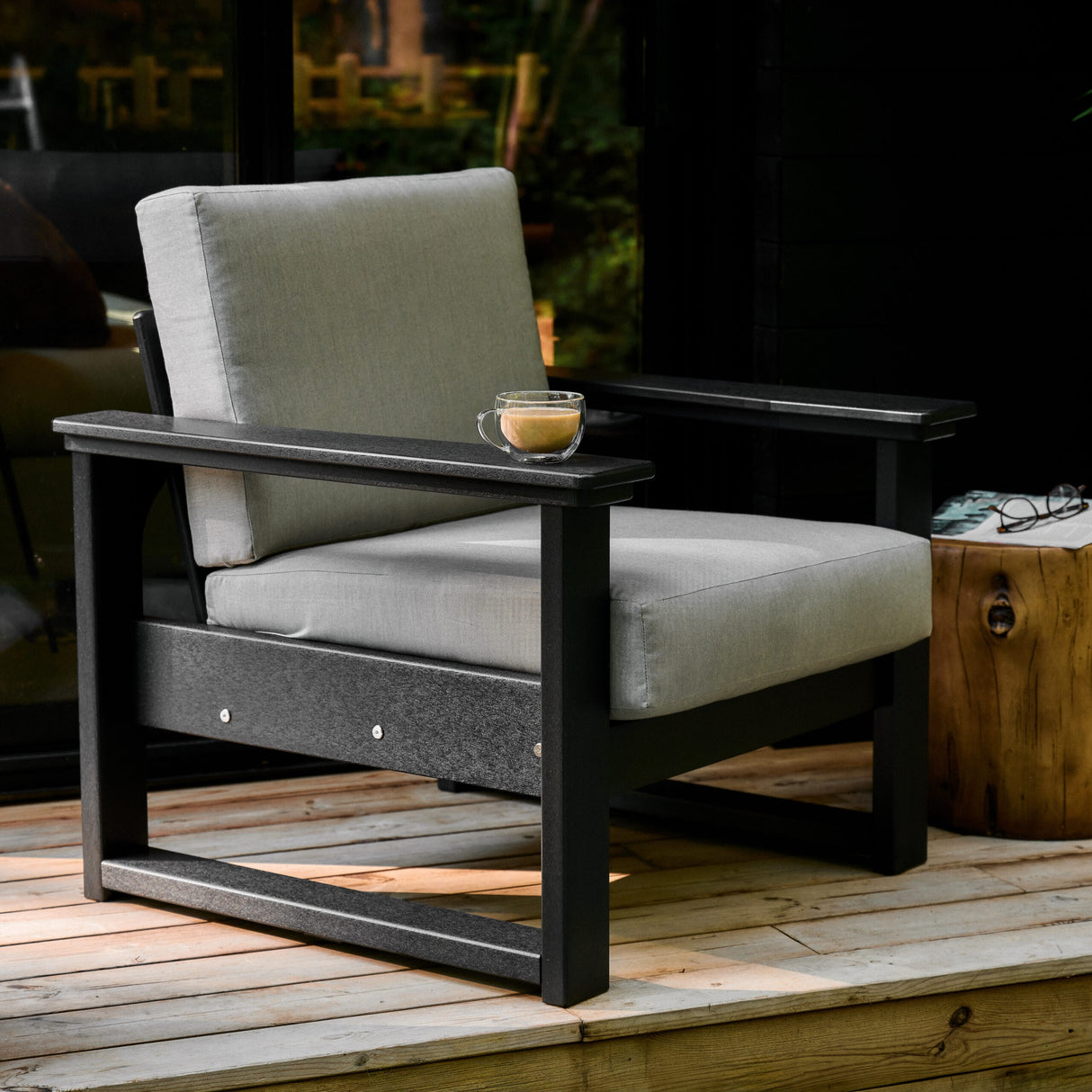 This is a lifestyle image showing a deep seating chair on a wooden patio. The frames are black and the cushions are Spectrum Dove colored.