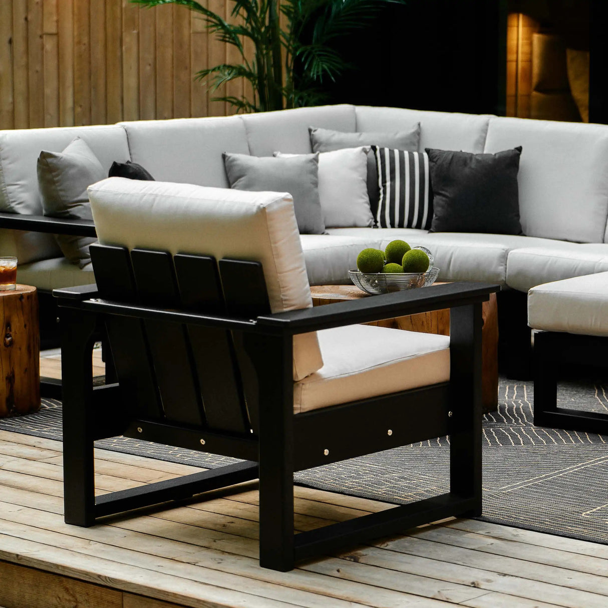 This is a lifestyle image showing a deep seating patio set on a wooden porch. The frames are Black and the cushions are Canvas colored.