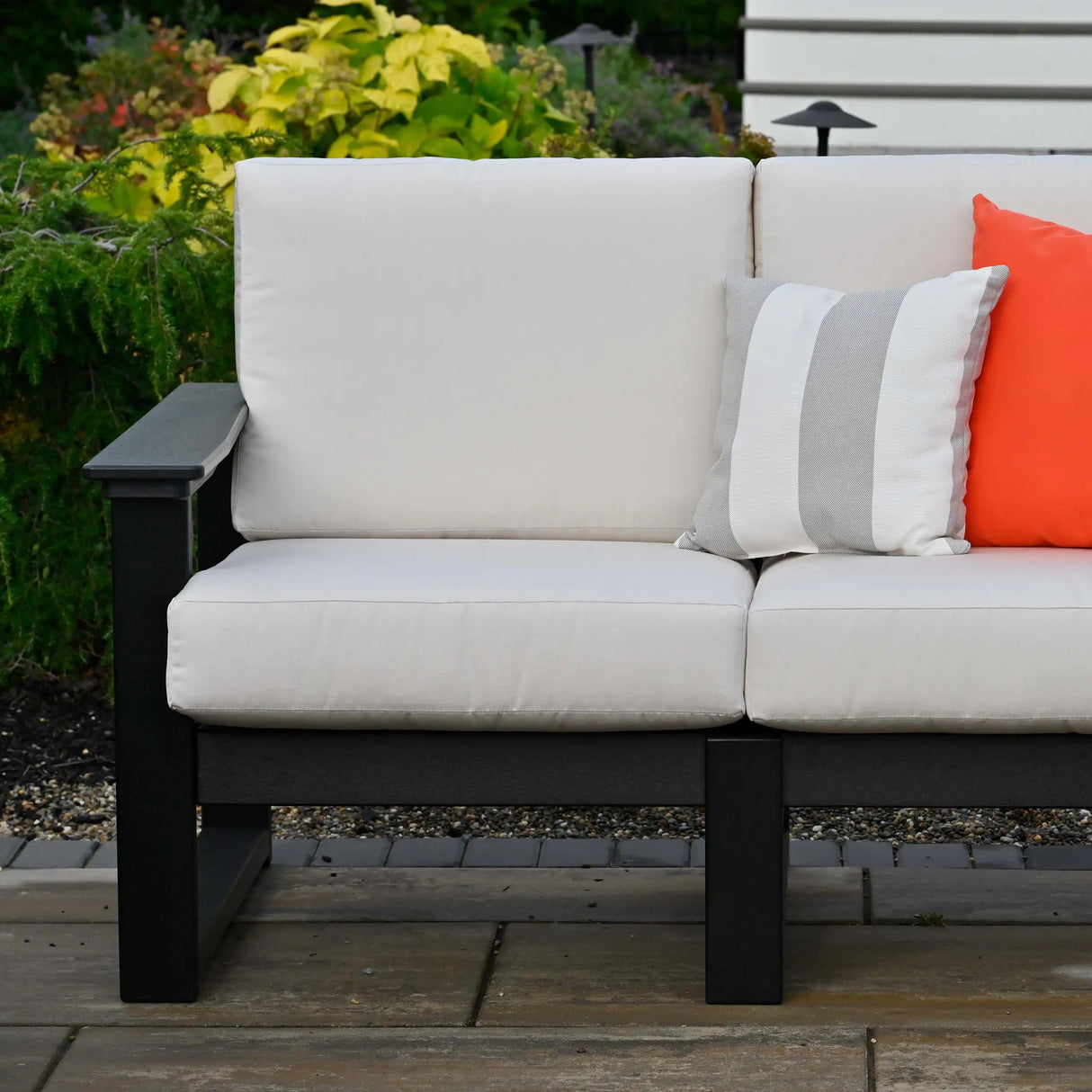 This is a lifestyle image showing a corner of a loveseat with black frames and canvas colored cushions.