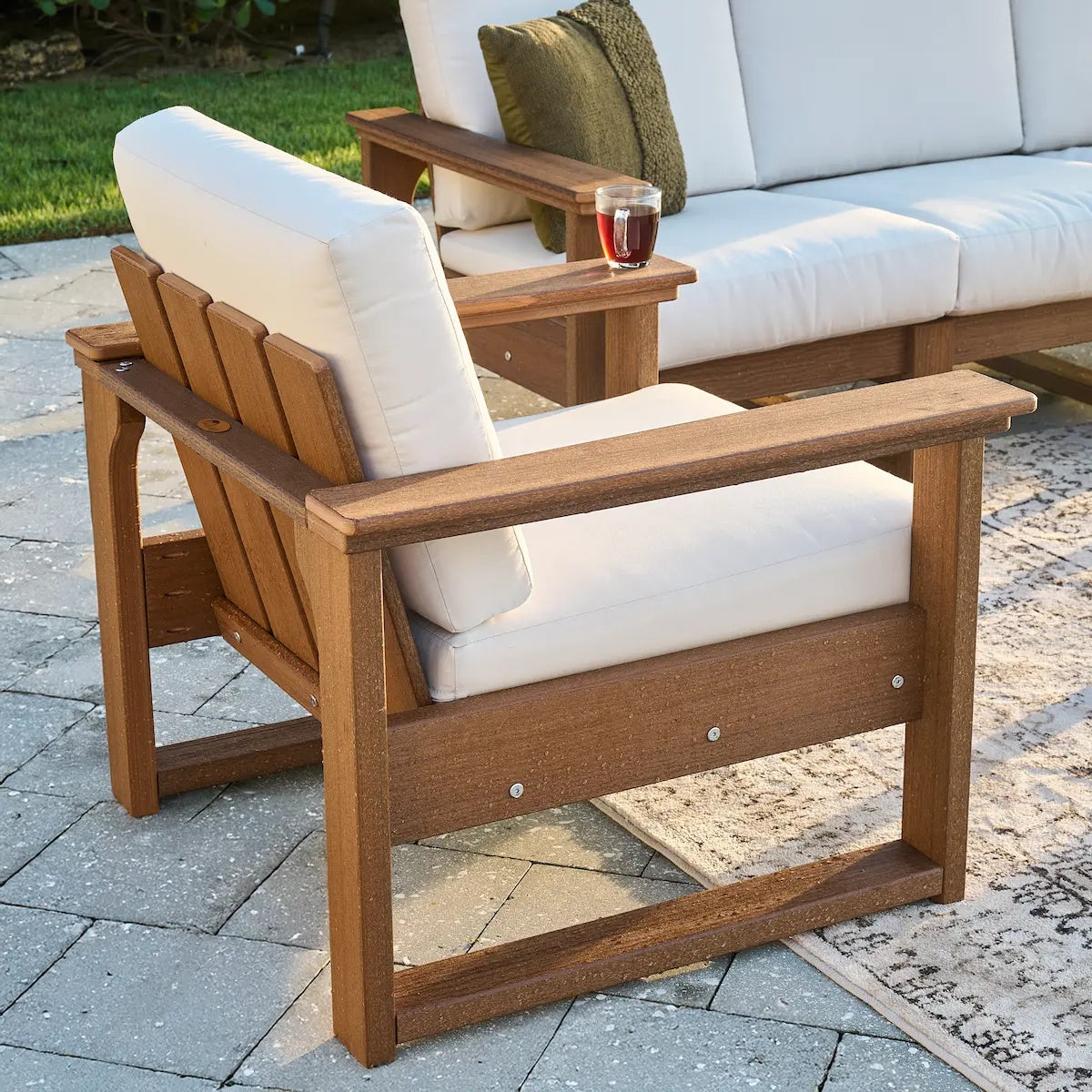 This is a lifestyle image showing the deep seating chair on a stone patio on an outdoor carpet. The frames are antique mahogany and the cushion is canvas.