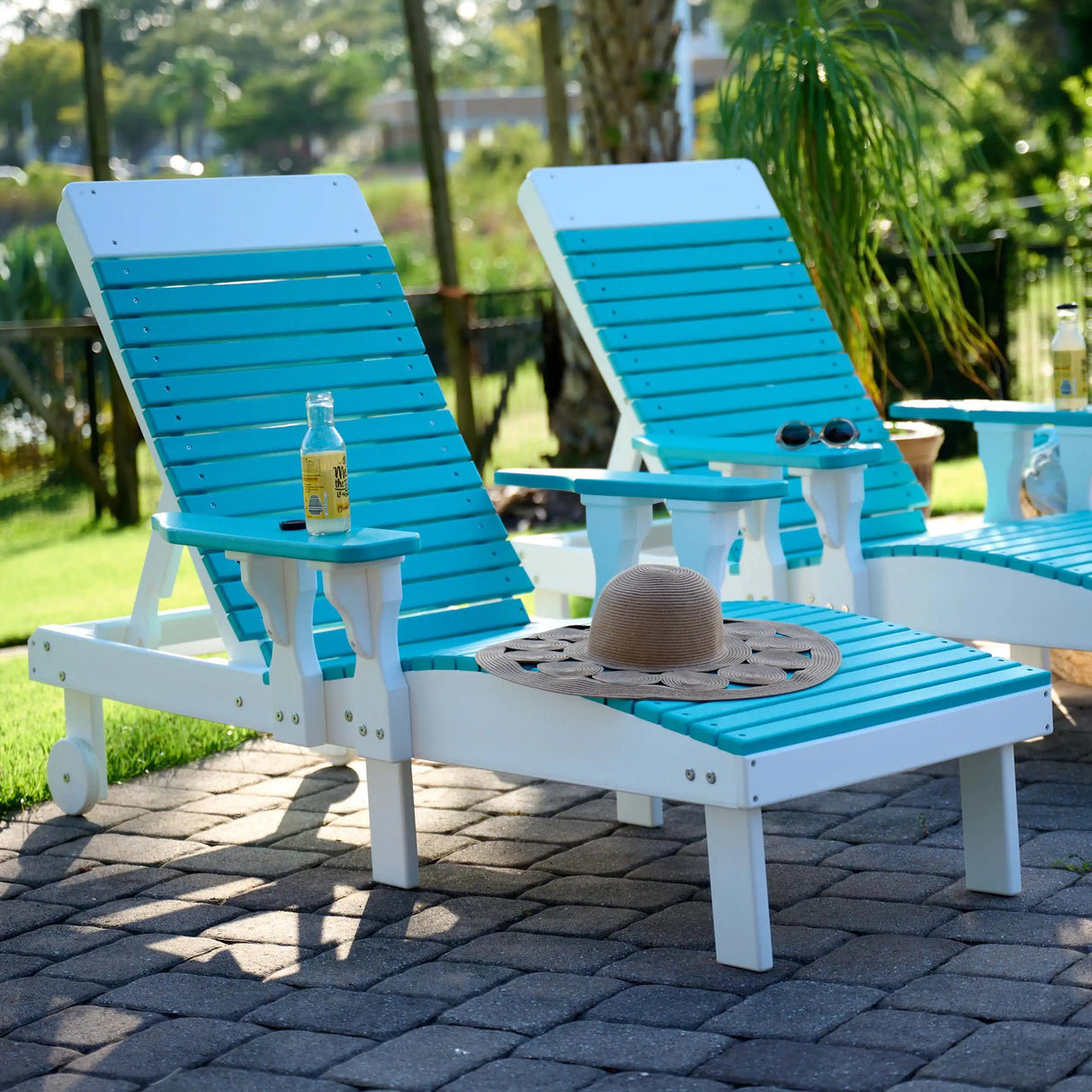 This is a lifestyle image showing two Aruba Blue and White colored lounge chairs on a stone patio in a grassy backyard.