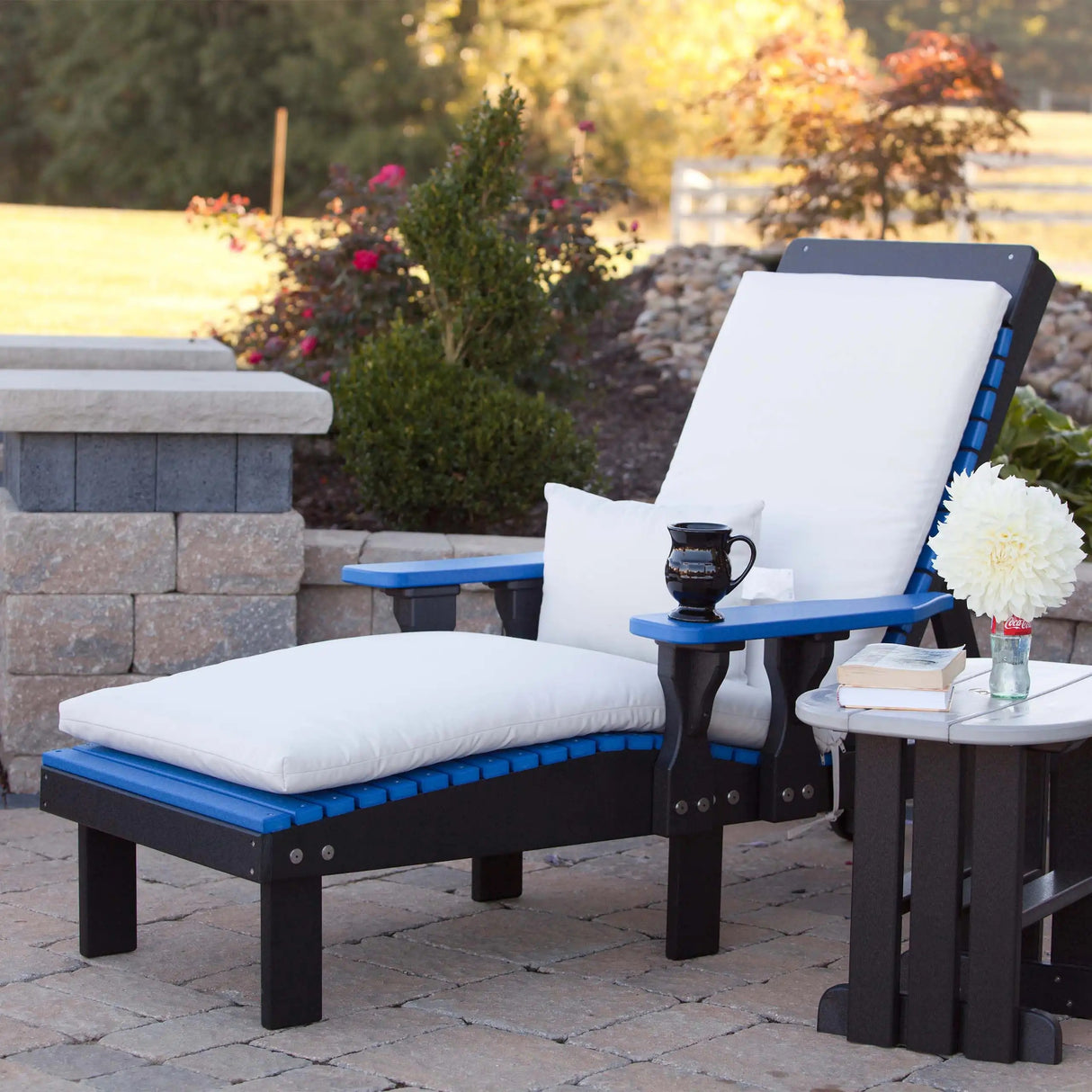 This is a lifestyle image showing a Blue and Black colored lounge chair on a stone patio. There's a lounge chair cushion on the chair (those are sold separately).