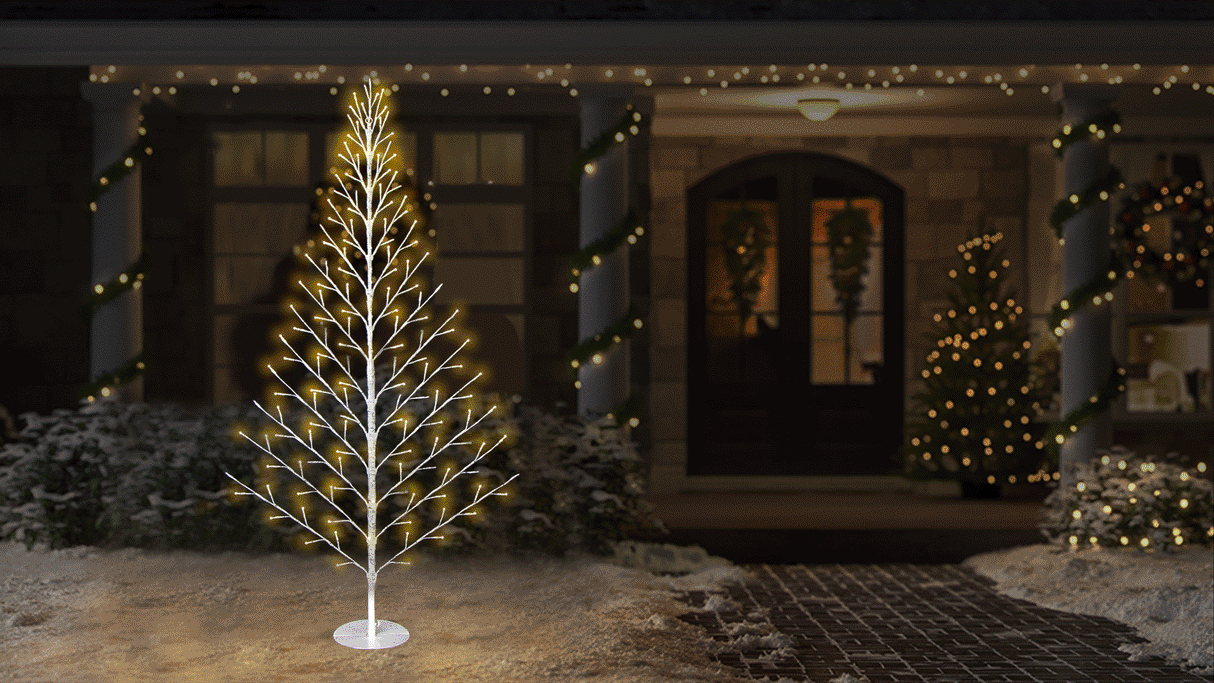 This animated image shows the birch wall tree on a snowy front lawn in front of a house decorated for Christmas.