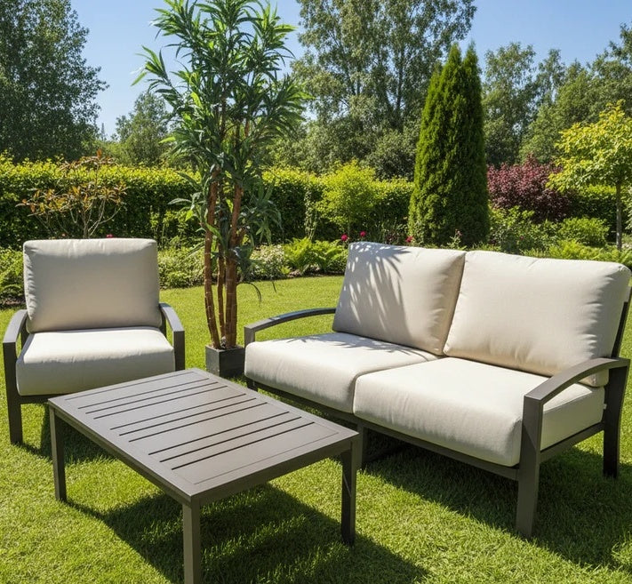 This is a lifestyle image showing this cushioned patio furniture in a grassy backyard on a sunny day with a potted palm tree next to it.