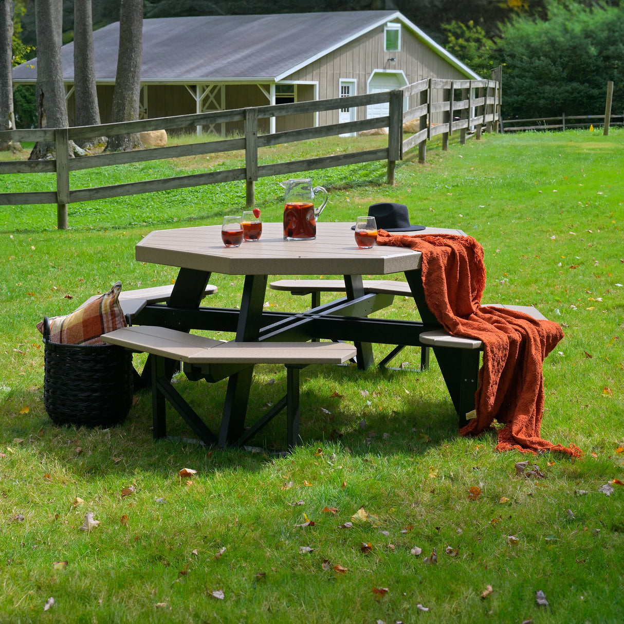 This is a lifestyle image showing the Weatherwood and Black colored picnic table with attached benches. It's in a grassy field and you can see a barn in the background.