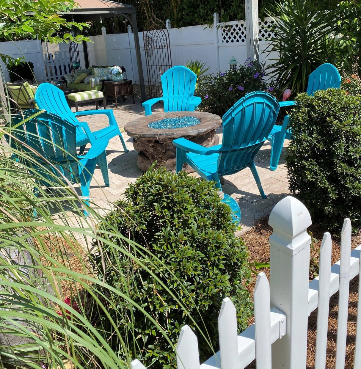 Five blue Adirondack chairs around a fire pit in a backyard.