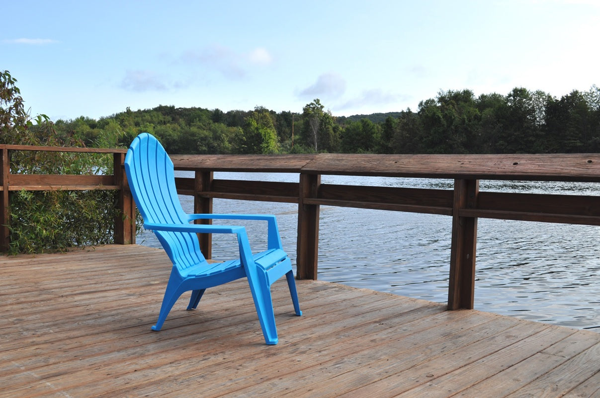 A blue Adirondack chair on a dock near a lake.