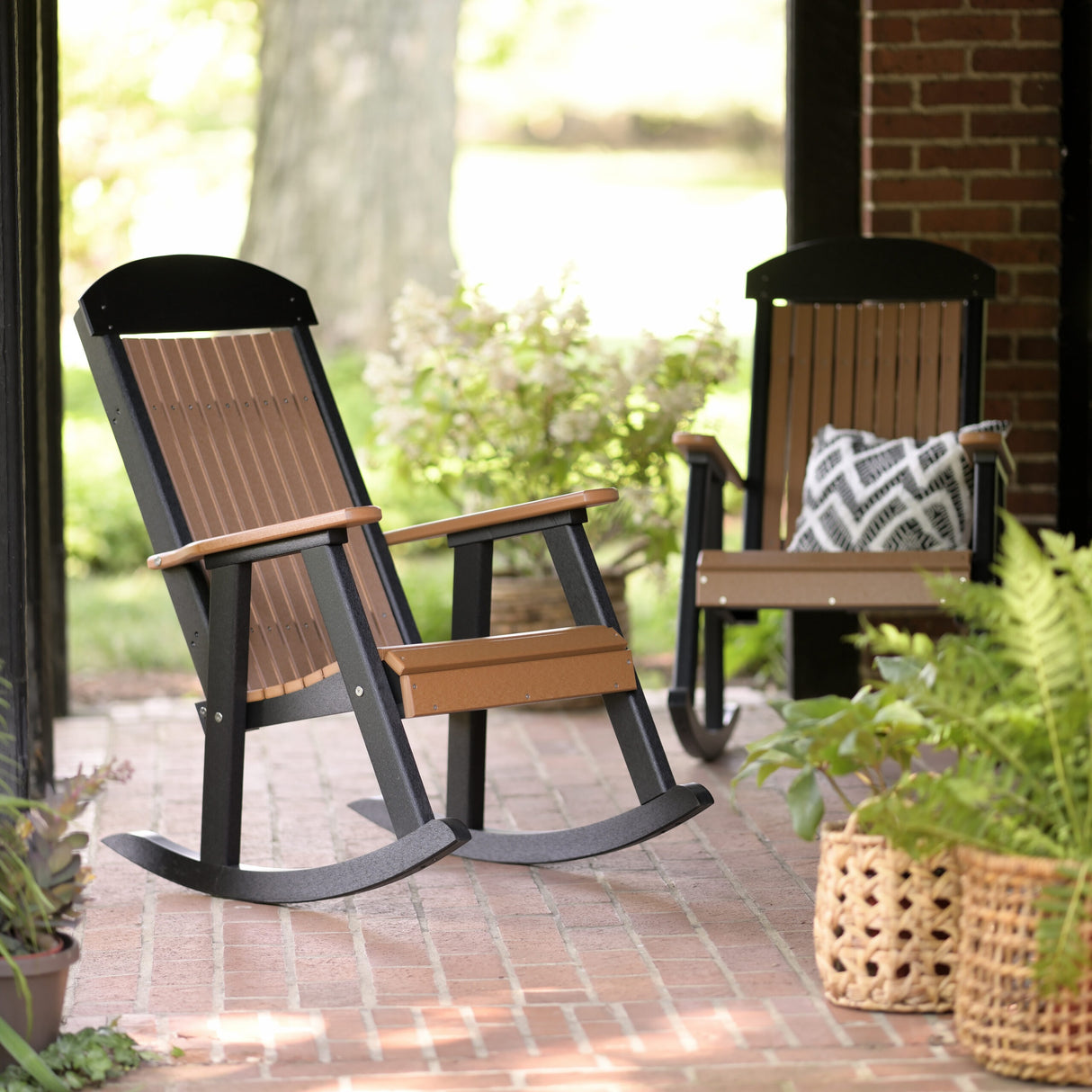 This is a lifestyle image showing two Antique Mahogany and Black colored Porch Rocker chairs on a brick patio.