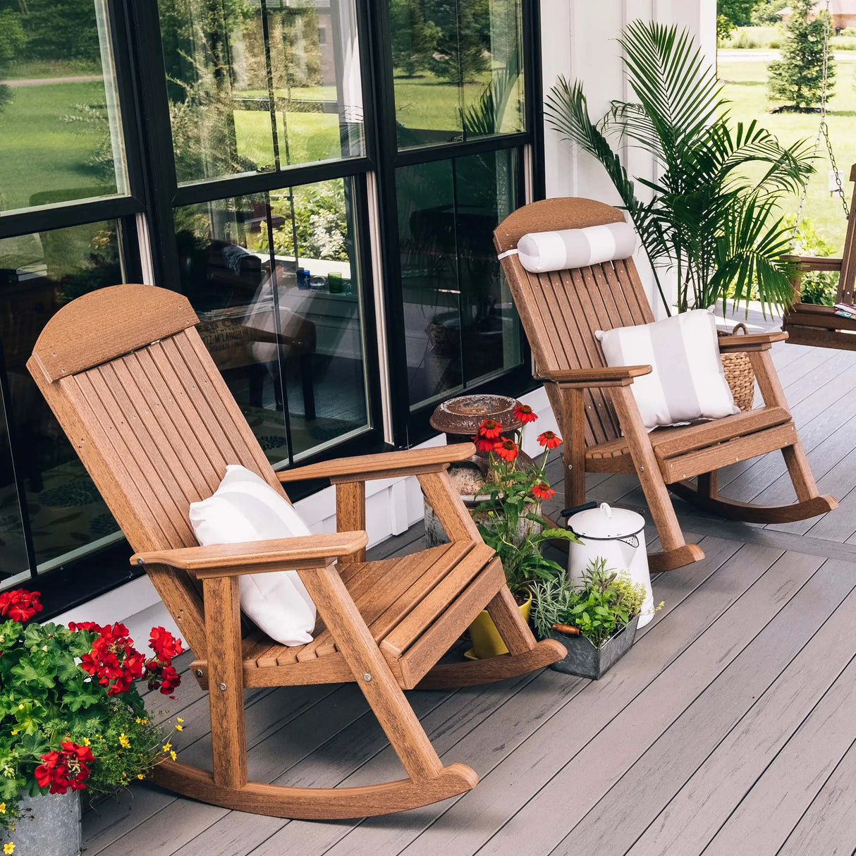 This is a lifestyle image showing two Antique Mahogany porch rocker chairs on a wooden porch in front of a glass window.
