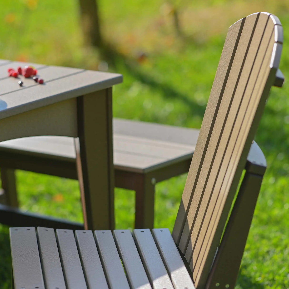 This is a lifestyle image showing an up close view of the Weatherwood and Chestnut Brown colored Adirondack side chair.