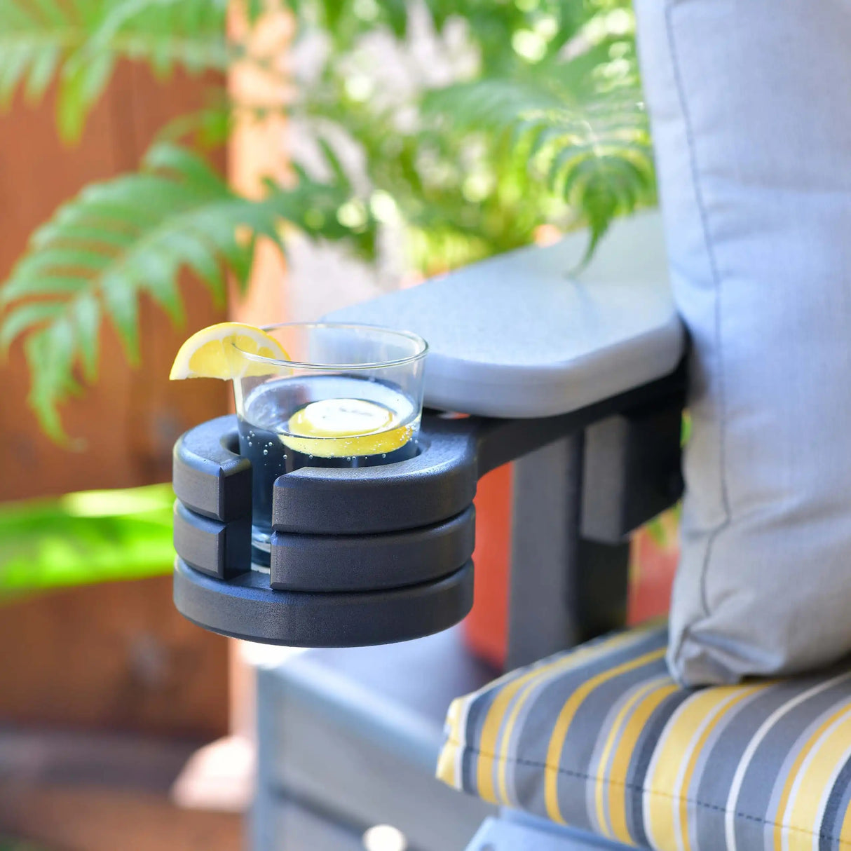 This is a lifestyle image showing the Black colored cup holder attached to the arm of a chair. Inside the cup holder, there's a glass cup with juice and lemons in it.