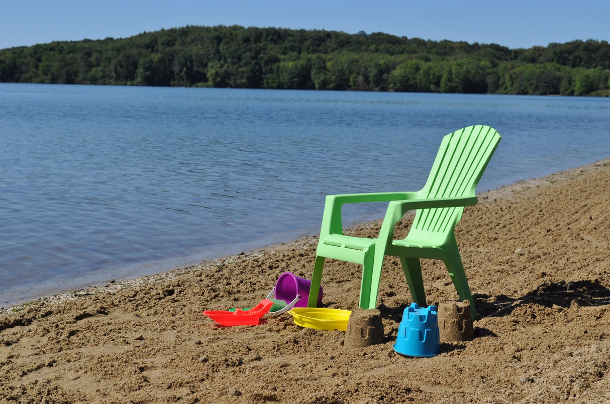 A lime green Adirondack chair on a beach near a lake.