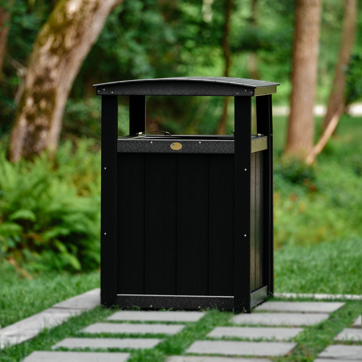 This is a lifestyle image showing the Black colored trash can on a grassy patio.