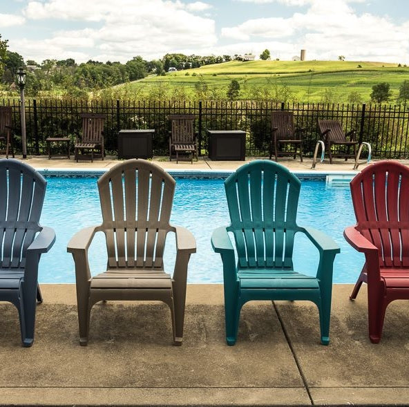 A few different colored Adirondack chairs near a pool.