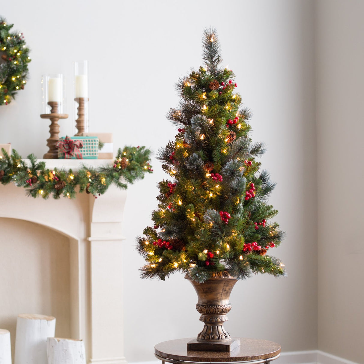 Artificial tree in a bronze pot pre-lit with clear lights. Some of the branches have white glitter on them. There are pine cones and berry accents.