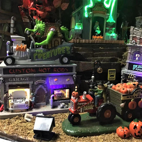 Polyresin and porcelain building for a Lemax Spooky Town display. Designed to look like a mechanic who does custom paint jobs for cars. There's a large green monster on the top, driving a giant car shaped like a house. The sign on the sign of the building reads "THE CREATURE'S."