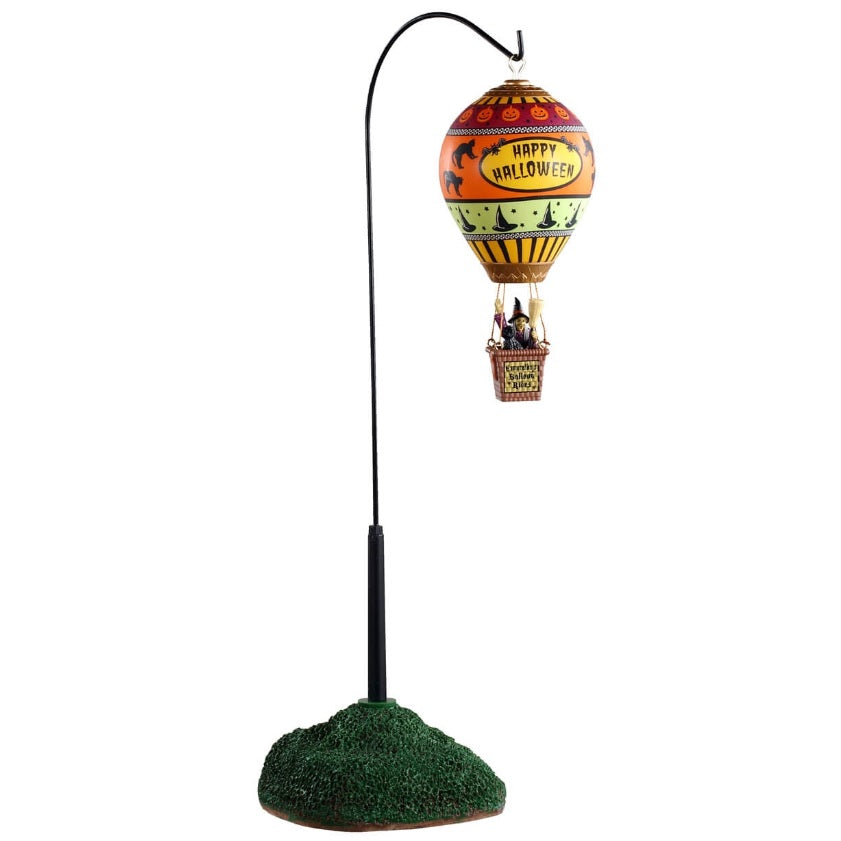 Polyresin carnival ride for a Lemax display. Designed to look like a hot air balloon with a lot of Halloween figures features on it. Things like pumpkins, witch hats and black cats. The colors on the hot air balloon are yellow, black, red, orange, light green and white. The basket underneath the balloon has a witch holding a broom.