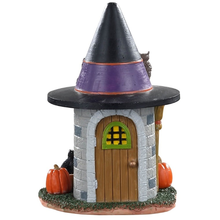 Small polyresin building for a Lemax Spooky Town display. Designed to look like a circular stone building with a witch hat for a roof. There are orange pumpkins on the side. This is the view of behind the building. There's a wooden door with a green window.