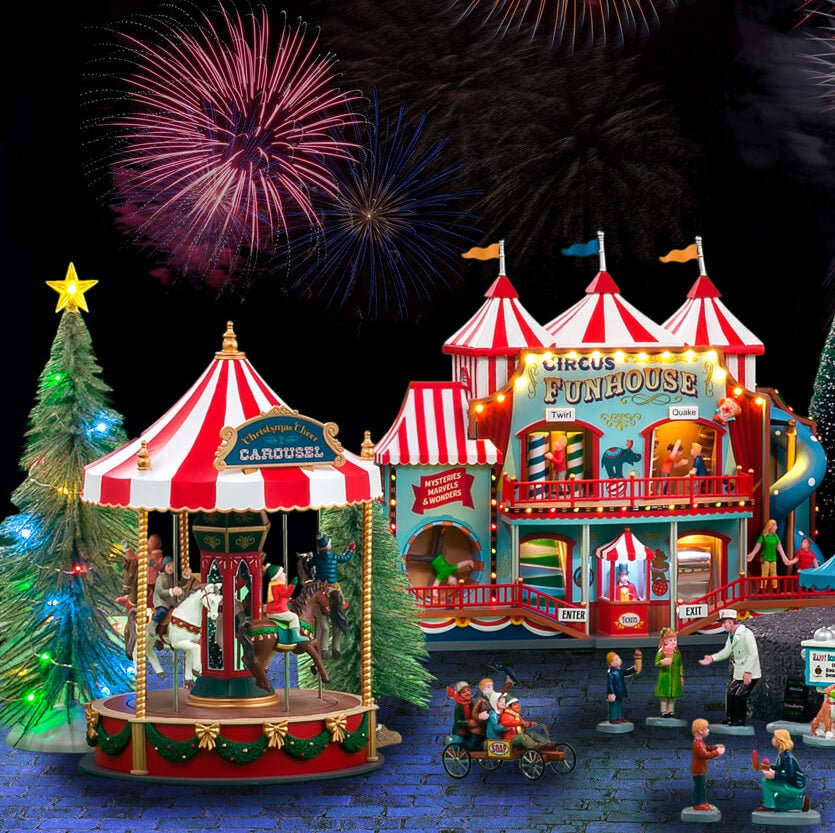 A collection of Lemax items in a tabletop display. There's a carousel and a Circus Funhouse with people doing various things off to the side with fireworks in the sky