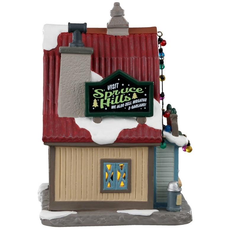 The side of a porcelain lighted building for a Lemax Village tabletop display. Sign on the side of the building reads "Visit Spruce Hills. We also sell wreaths and garland!"