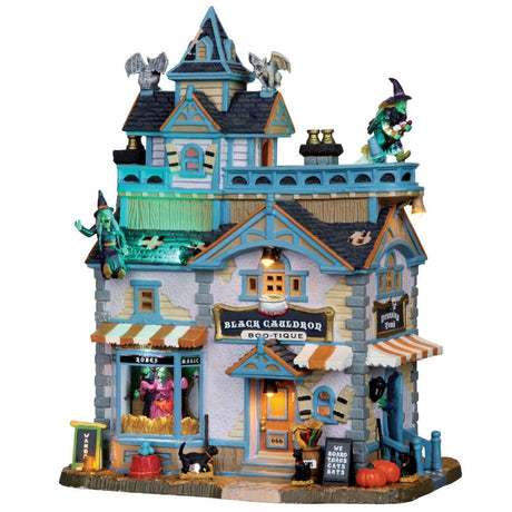Porcelain lighted building for a Lemax display. Designed to look like a boutique store. There are witches, gargoyles, pumpkins and black cats. Inside the window, you can see a monster trying on a pink dress.