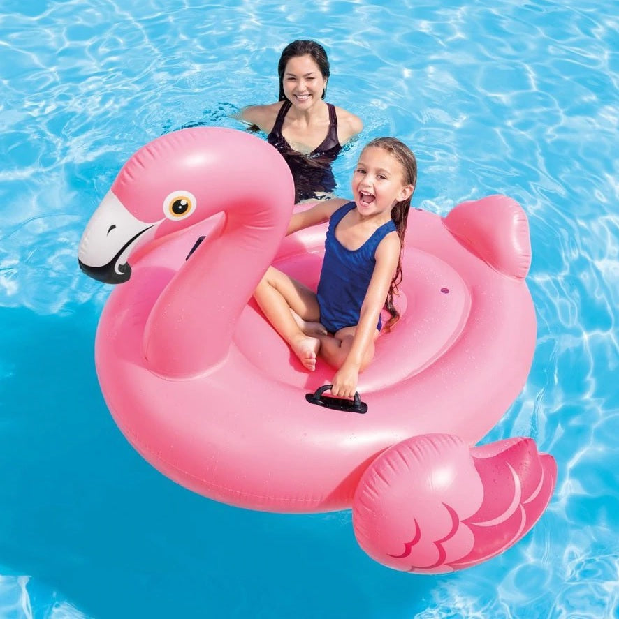 This is a lifestyle image showing a young girl sitting on the flamingo float while her mom looks on.